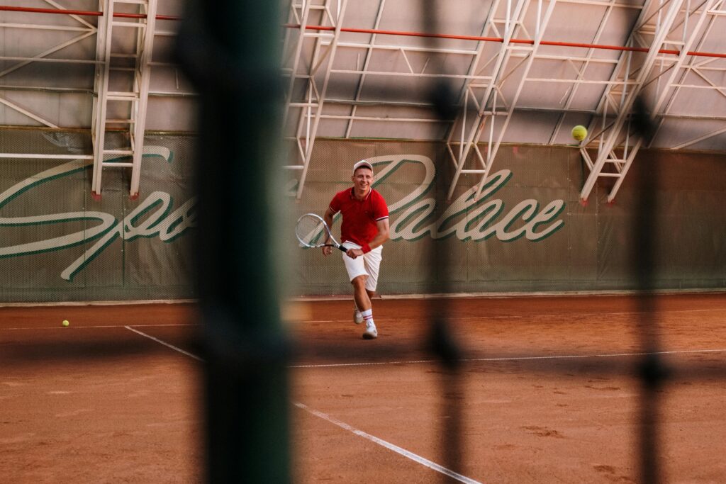 pexels-photo-5740521-5740521 A male tennis player in action on a clay court at Sports Palace indoor facility.